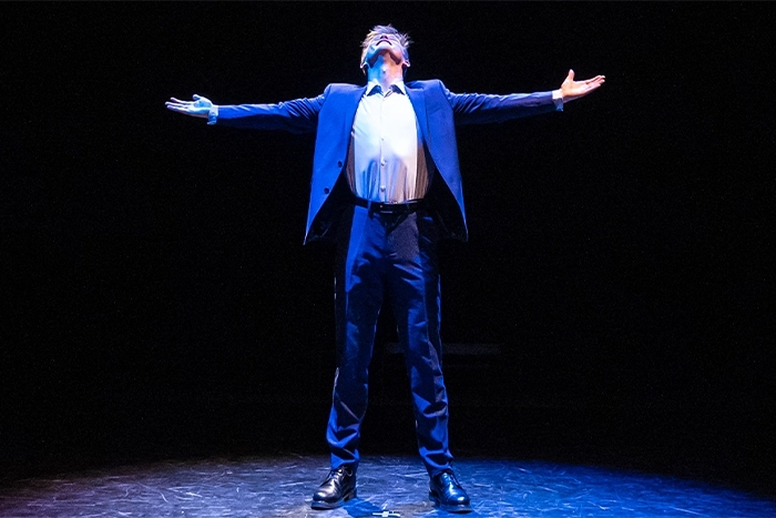 Man on stage looking up with outstretched arms
