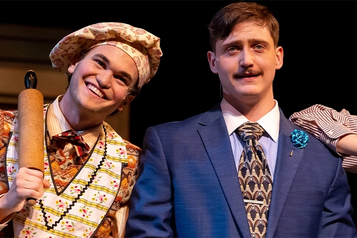Two men, one in chef's hat and another in a suit on stage